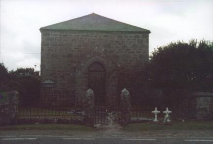 An austere roadside chapel with two small white cross memorials outside the gate