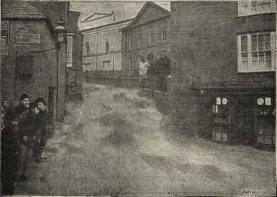 Torrents of water flooding down the narrow street - onlookers huddled close to the walls