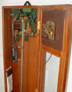 internal view of Gent clock with green and bronze mechanism
      at the top and separate slave dial mechanism attached to the door