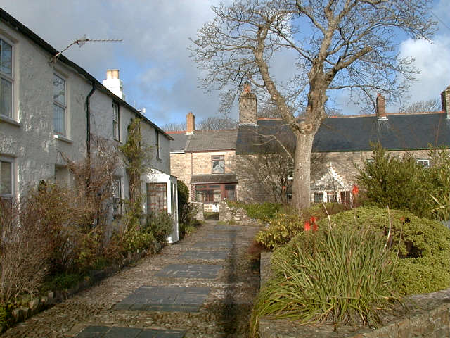 Terraced cottages to the left of a walkway with stone walled gardens to the right. In the background are other cottages.